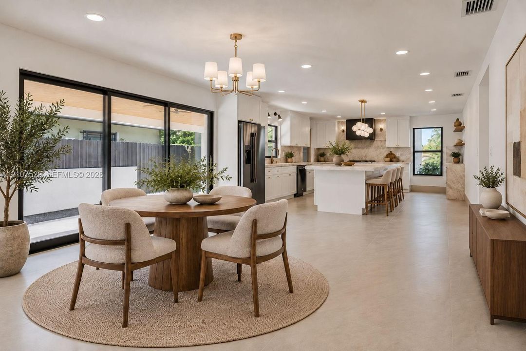 Open-concept interior featuring a center island with quartz countertops, custom white cabinetry, recessed lighting, multi-arm chandeliers, and large-format sliding glass doors