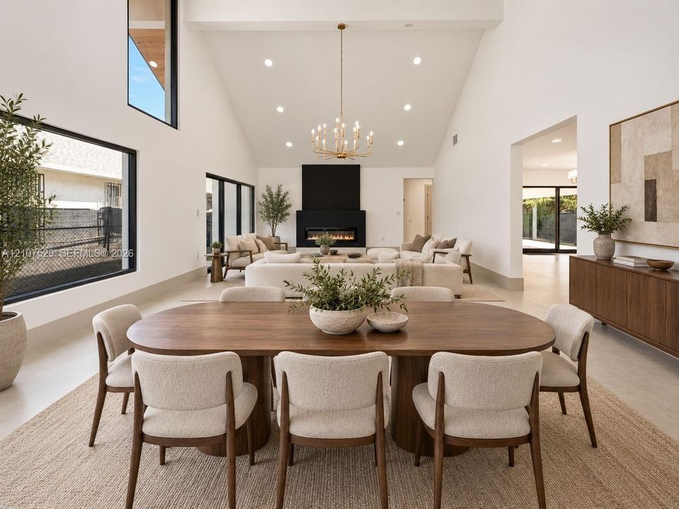 Vaulted ceilings, expansive black-trimmed windows, linear fireplace with a floor-to-ceiling surround, recessed lighting, and a tiered metal chandelier