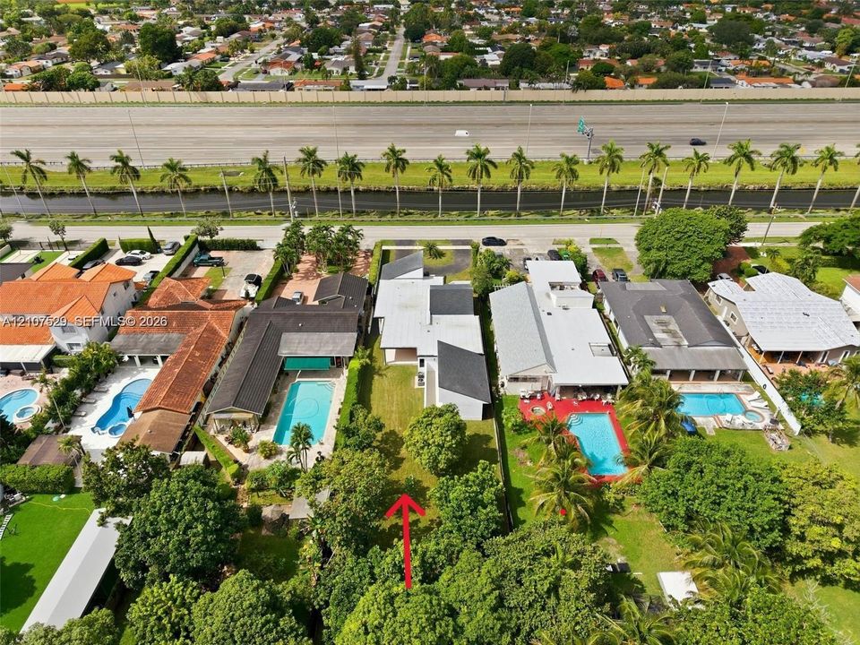 Aerial perspective of the property featuring a direct canal frontage, paved driveway, mature palm trees, and residential surroundings