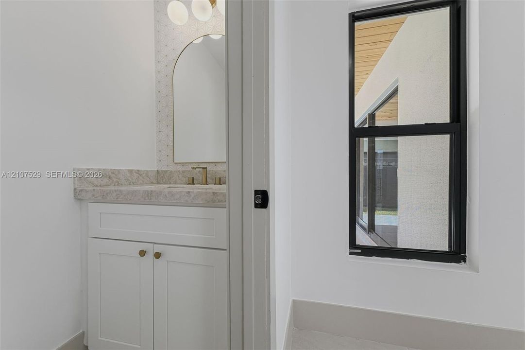 Dual-vanity cabinetry with stone-finish countertops, arched vanity mirrors, multi-bulb lighting, wall-mounted matte black faucet, and a freestanding soaking tub