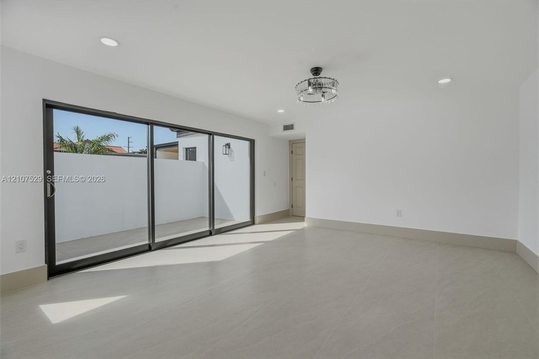 Modern exterior patio featuring large-format porcelain tile flooring, expansive floor-to-ceiling sliding glass panels, smooth white stucco finish, and a private enclosed yard