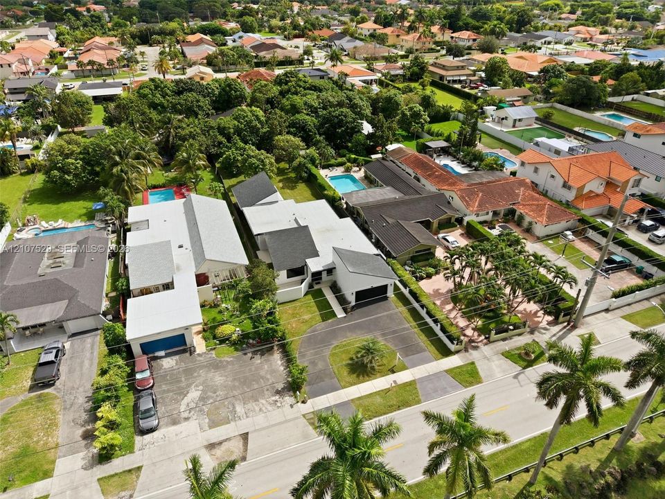 Aerial perspective of a residential street featuring mature palm tree landscaping, paved driveways, and waterway access