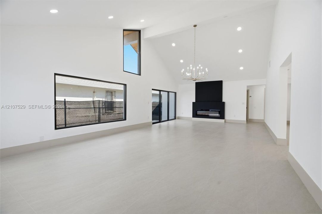 Open-concept interior featuring vaulted ceilings, large-format tile flooring, recessed lighting, and a panoramic picture window