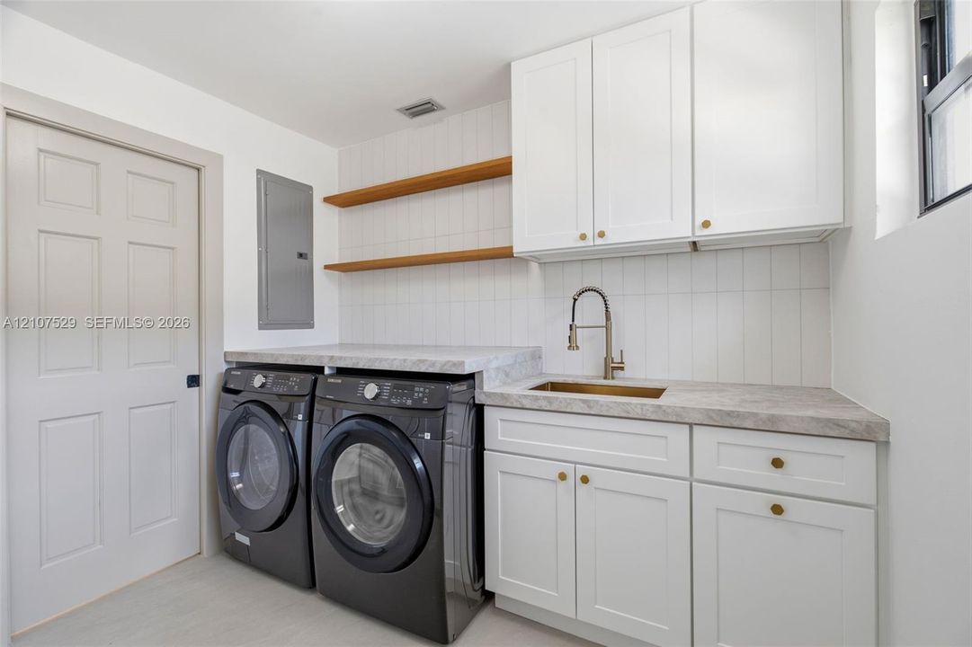 White shaker-style cabinetry with brass-tone hardware, stone-finish countertop, neutral large-format flooring, and drum-style ceiling fixture