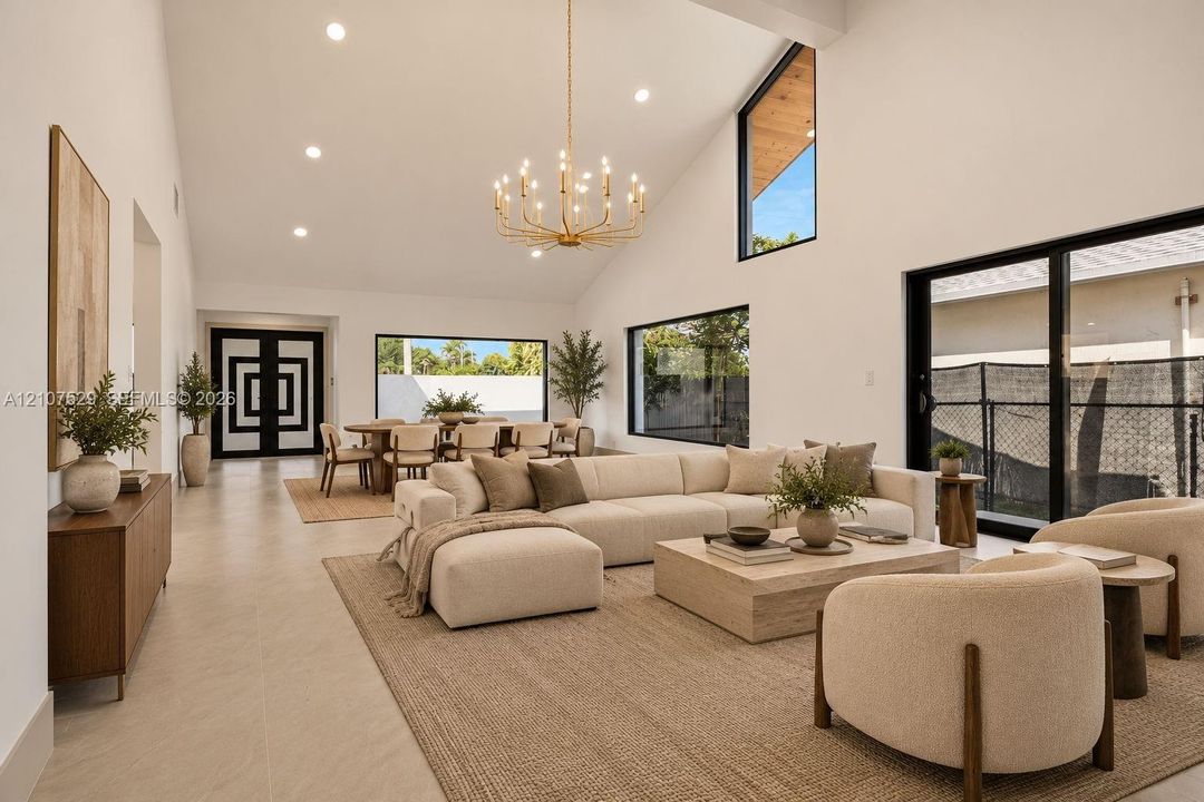 Vaulted ceilings featuring recessed lighting and a multi-tiered gold-tone chandelier, complemented by large-format neutral tile flooring and geometric paneled double entry doors
