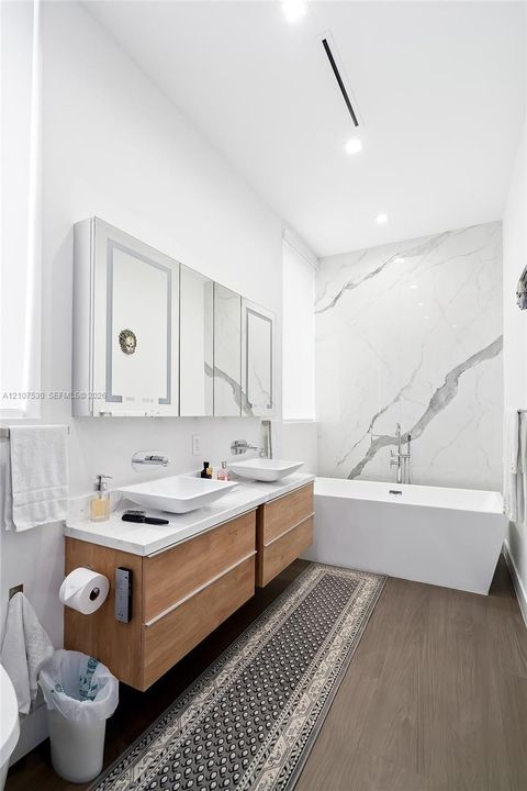Floating wood-finish double vanity with rectangular vessel sinks, quartz countertop, mirrored medicine cabinets, and floor-to-ceiling stone slab wall feature with soaking tub