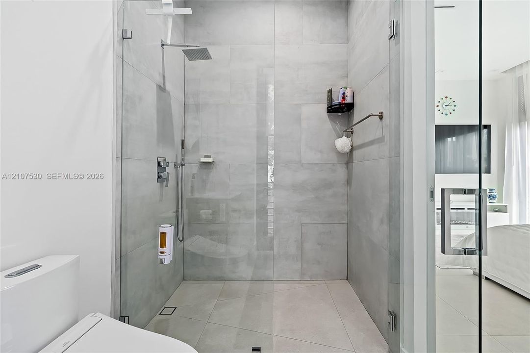 Walk-in shower featuring large-format grey tile, a frameless glass enclosure, a rainfall showerhead, and a wall-mounted chrome fixture set