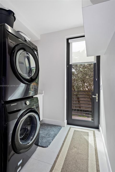 Laundry area featuring stacked appliances, a solid-surface countertop, cabinetry, and a full-height glass-panel door