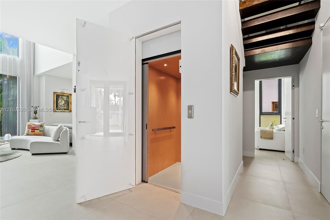 Residential elevator featuring a wood-paneled interior and metal handrail, complemented by a white glass-paneled entry door and large-format tile flooring