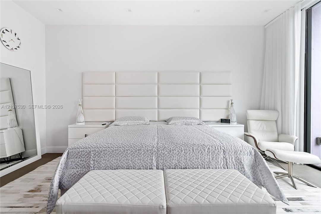 Full-height paneled headboard, recessed ceiling lighting, and floor-to-ceiling glass panel with drapery