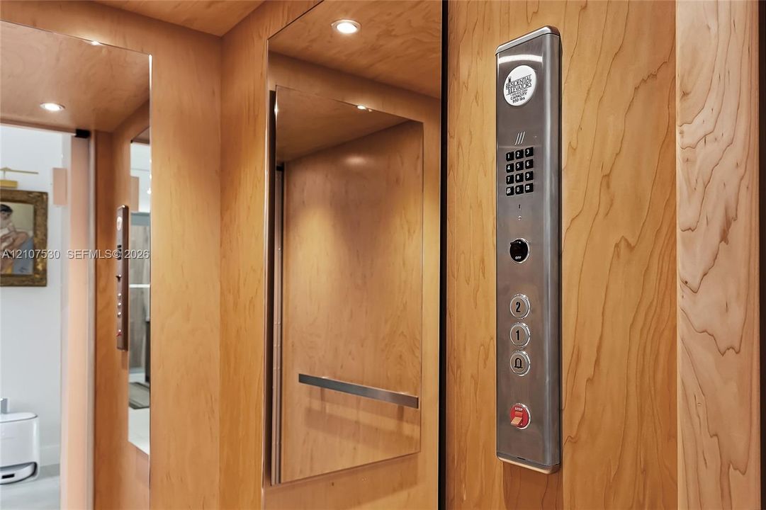 Elevator interior featuring wood-finish paneling, inset mirrored panels, recessed lighting, and a stainless steel control interface with numeric keypad