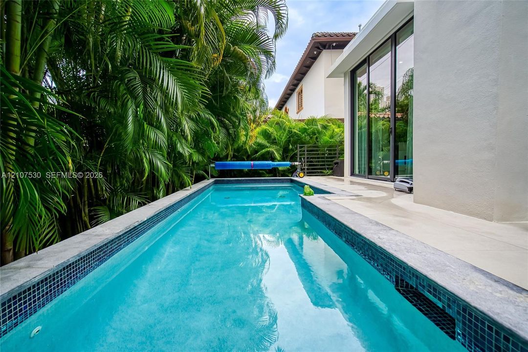 Rectangular lap pool featuring dark mosaic tile trim, concrete decking, and floor-to-ceiling sliding glass doors