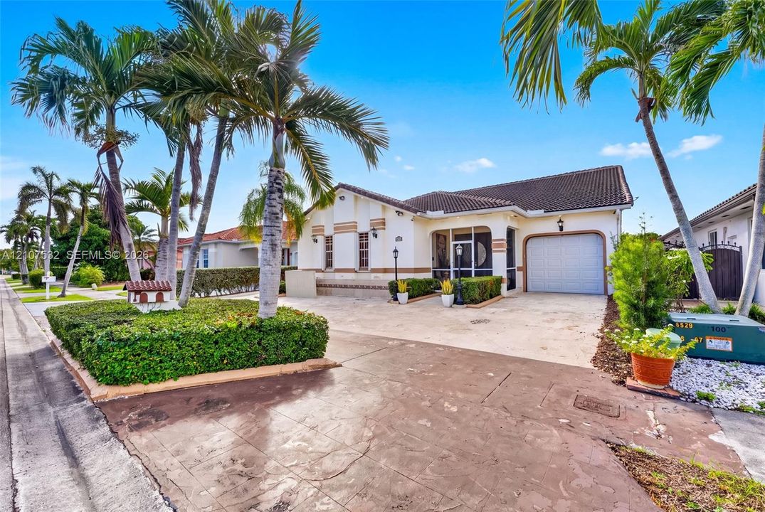 Single-story exterior featuring a light-toned stucco façade, a tiled roof, an attached garage, and mature palm trees