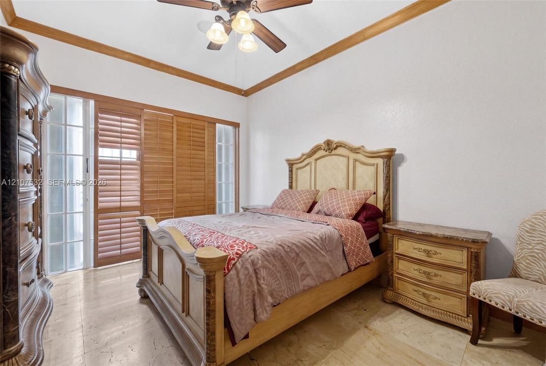 Tray ceiling with crown molding, natural stone flooring, and built-in sliding wood-slat closet doors with sidelight windows