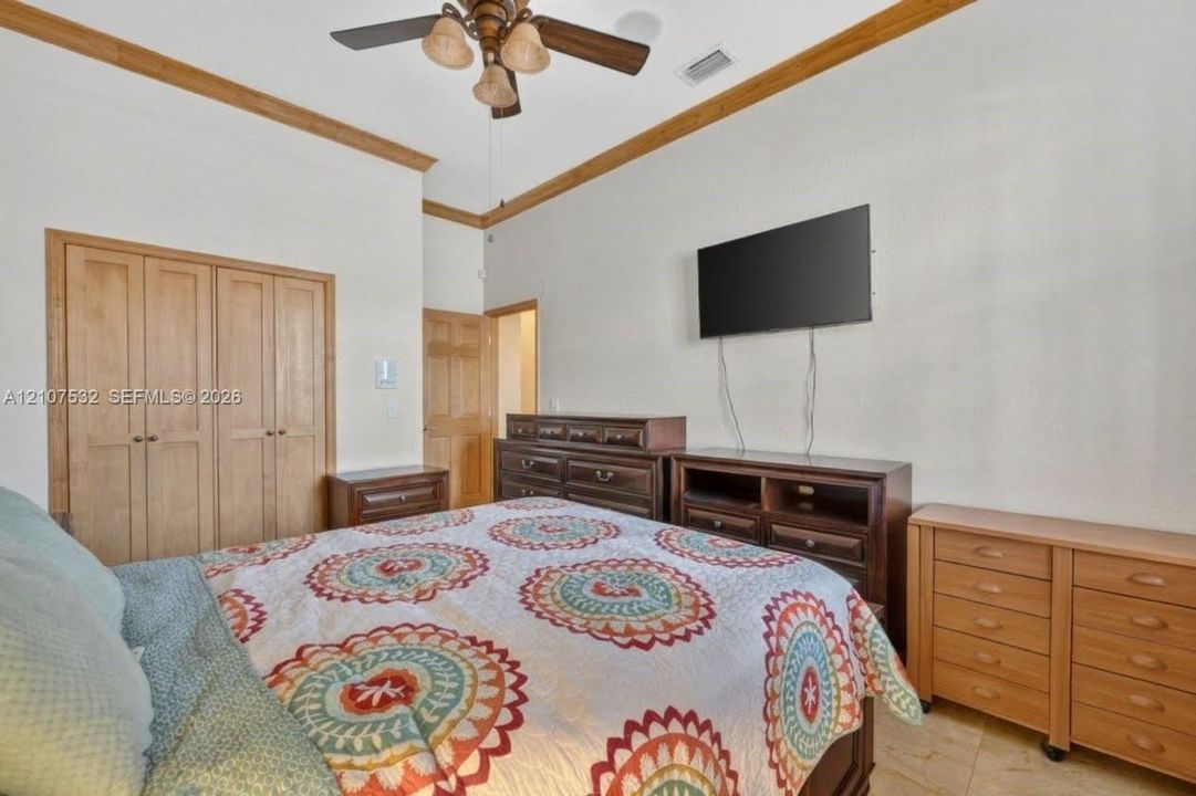 Room featuring crown molding, multi-panel wood doors, tile flooring, and a ceiling fan with integrated lighting
