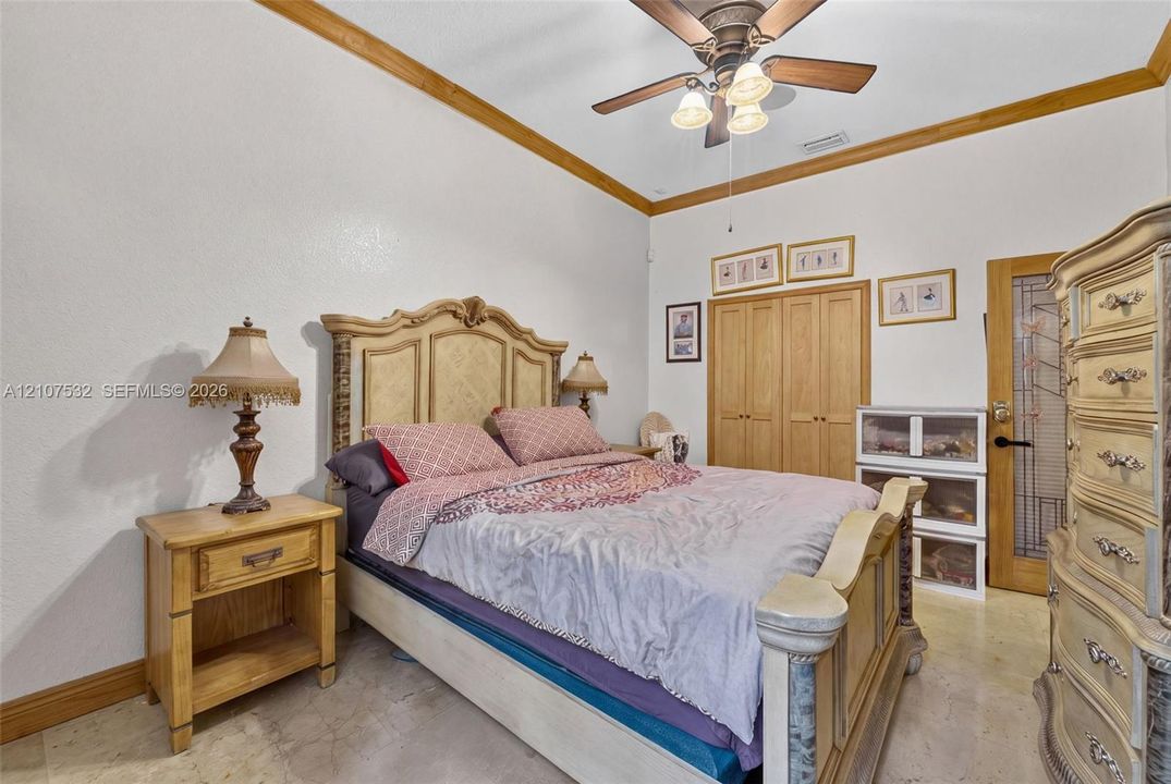 Vaulted ceiling featuring crown molding, neutral stone-finish flooring, ceiling fan with integrated light fixture, built-in wooden closet doors, and a door with decorative glass paneling