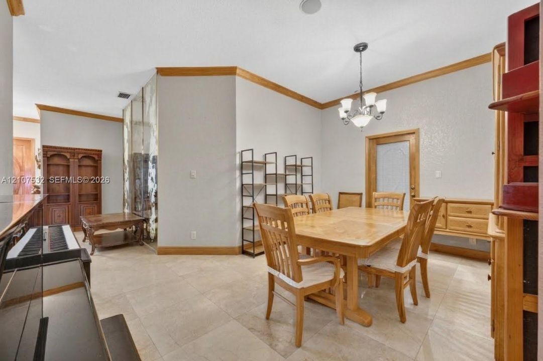 Large-format stone flooring, crown molding with natural wood finish, built-in wooden cabinetry, multi-panel mirrored wall, and overhead chandelier lighting