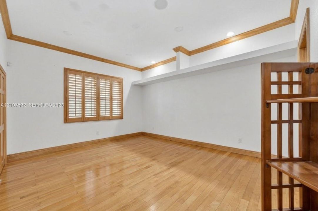 Interior space featuring wood-finish flooring, ceiling crown molding, wood-framed window shutters, recessed lighting, and a built-in recessed shelf