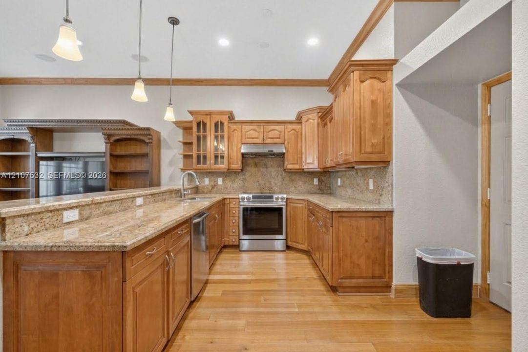 Kitchen featuring custom wood cabinetry, stone countertops, stainless steel appliances, wood-finish flooring, and three pendant light fixtures