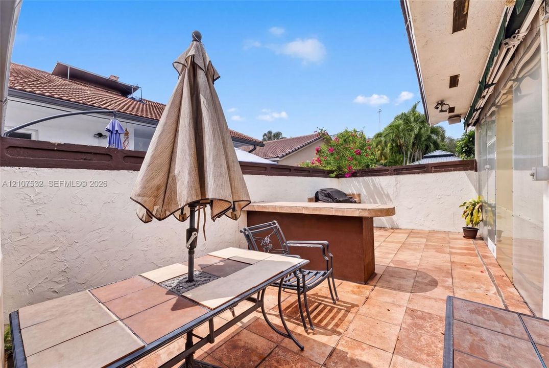 Enclosed patio featuring terracotta-style tile flooring, built-in bar, textured stucco perimeter walls, and an overhead structural awning