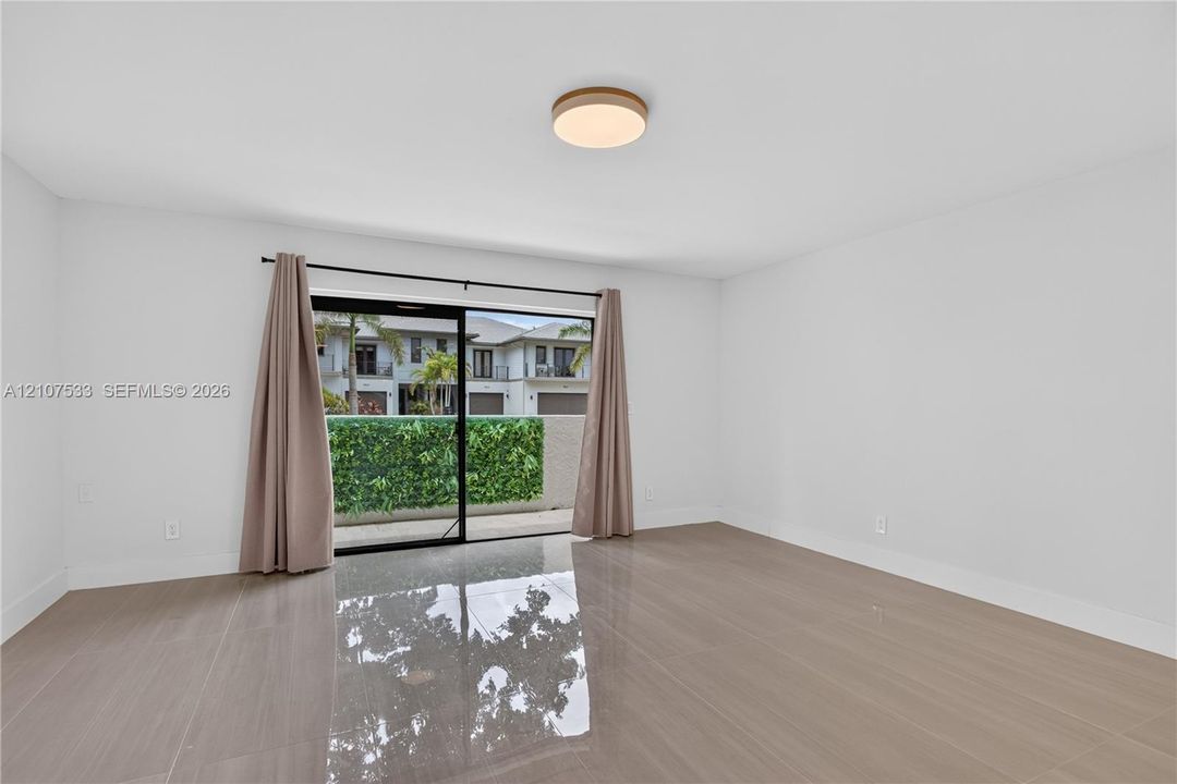 Interior space featuring large-format tile flooring, a circular flush-mount ceiling light, and sliding glass doors opening to a concrete patio with perimeter greenery
