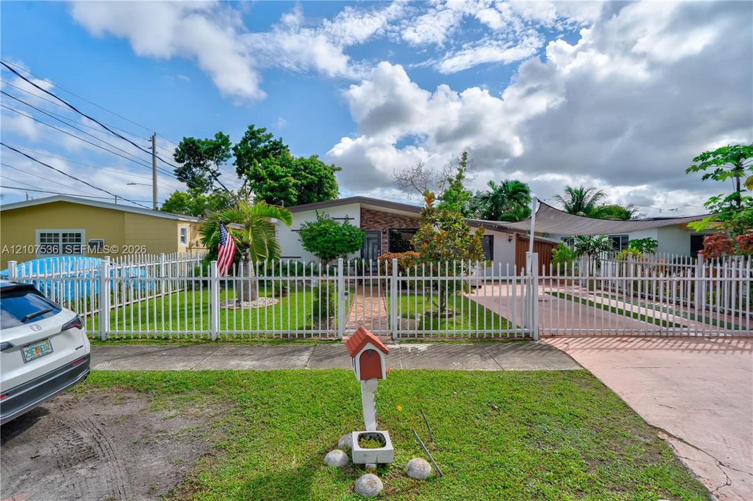 Single-story residence with a brick-veneer facade, gated front yard with a paved driveway, and a white aluminum perimeter fence