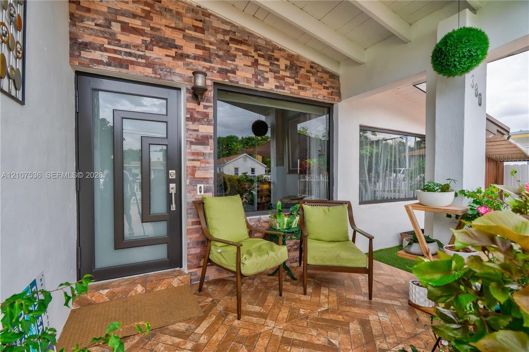 Covered front porch featuring herringbone-patterned masonry flooring, decorative stone-veneer siding, and a modern entry door with geometric glass paneling