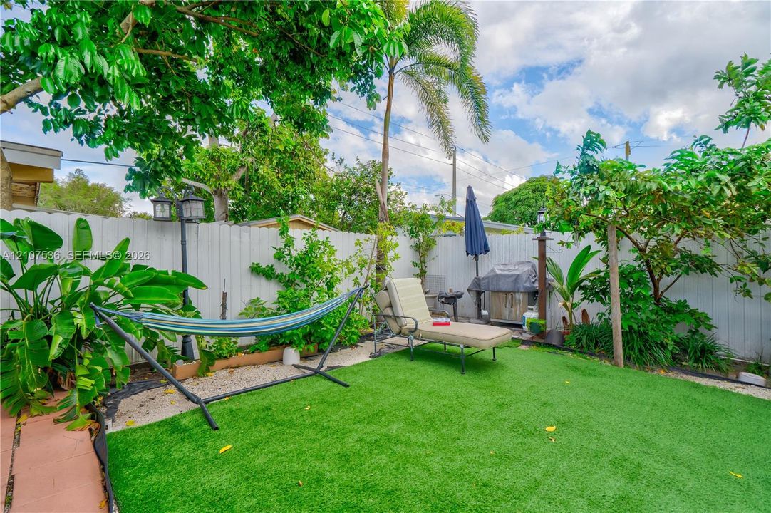 Enclosed backyard featuring synthetic turf, privacy fencing, mature trees, and dual post-mounted lighting fixtures