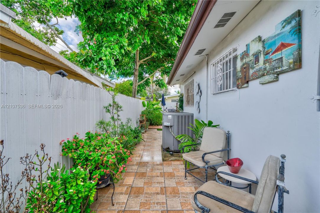 Side patio featuring patterned tile flooring, white privacy fencing, and mature landscaping