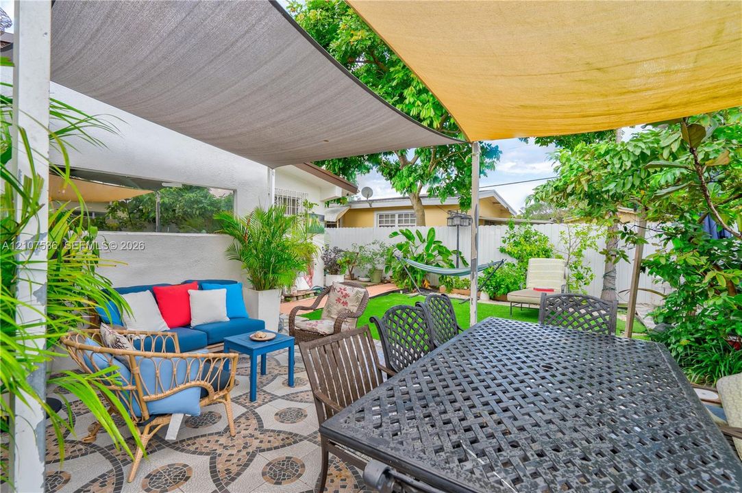Private backyard featuring a patterned stone patio, two overhead fabric shade sails, perimeter privacy fencing, and established greenery