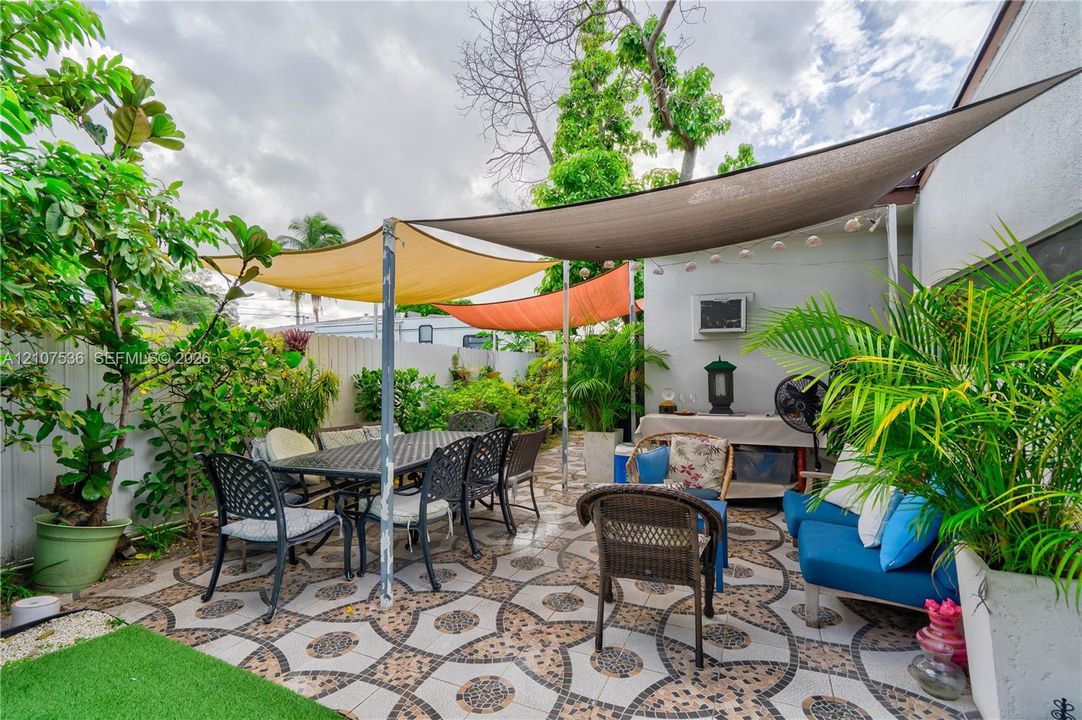Patio area featuring decorative patterned tile flooring, overhead shade sails, and perimeter fencing
