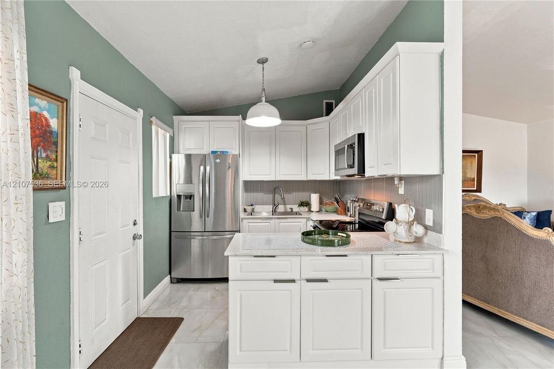 Kitchen featuring white shaker-style cabinetry, stone-finish countertops, stainless steel appliances, a center island, and tile flooring