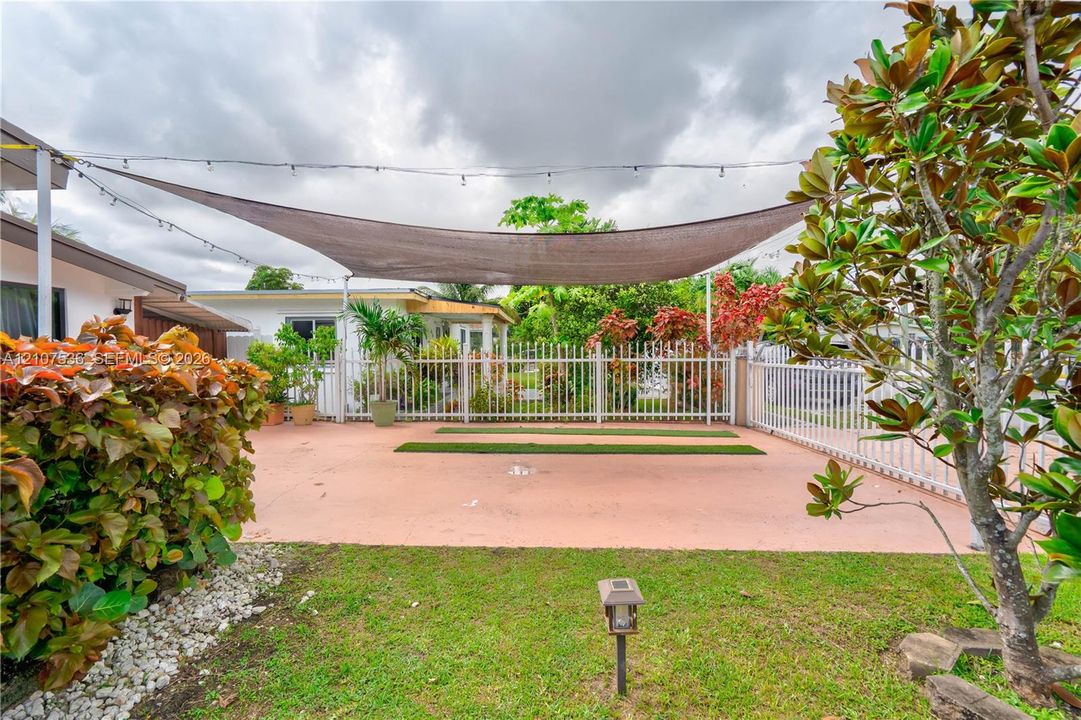 Outdoor patio featuring a concrete surface, overhead fabric shade structure, white picket-style fencing, and integrated landscape lighting