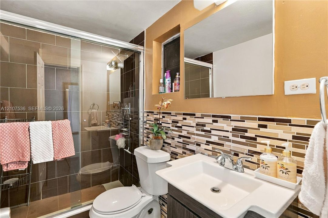 Bathroom featuring a glass-enclosed shower with large-format tile surround, vanity with an integrated basin, chrome dual-handle faucet, and multi-tonal mosaic tile backsplash