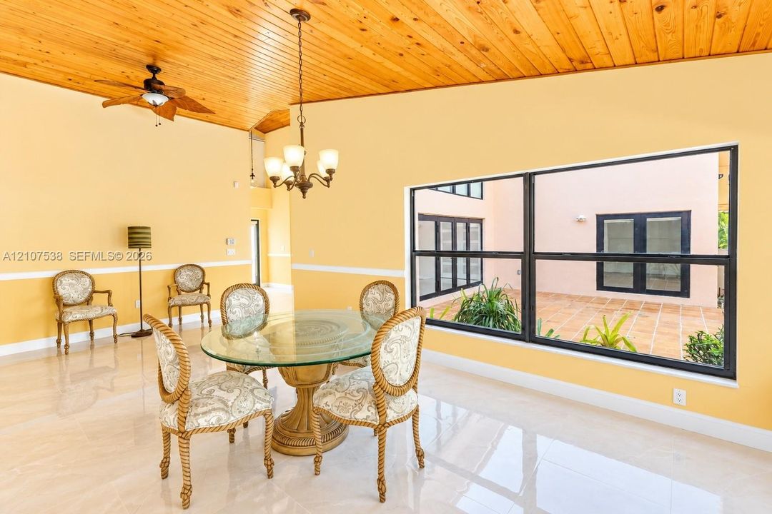 Vaulted wood-plank ceiling, polished tile flooring, prominent multi-pane window, and decorative hanging chandelier