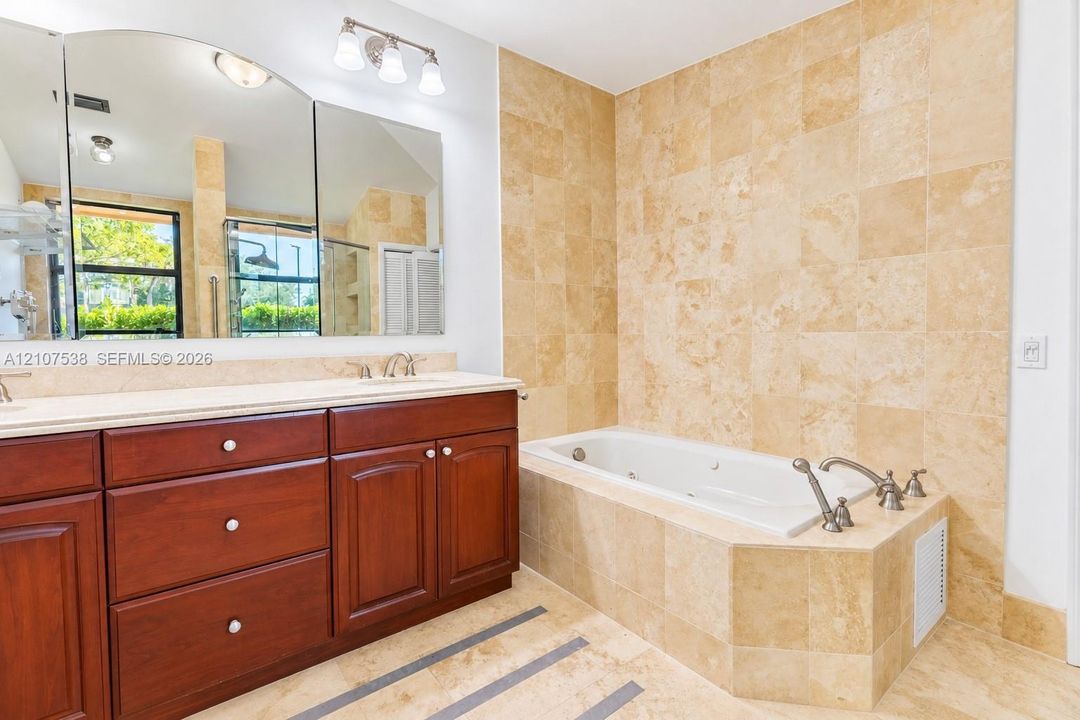 Built-in vanity featuring wood-finish cabinetry, countertop with dual undermount sinks, stone-tiled jetted tub surround, and wall-mounted three-light fixture