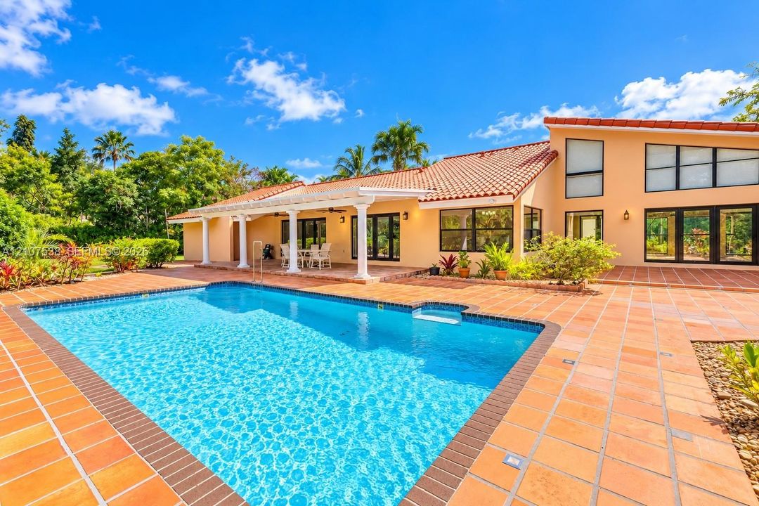 Swimming pool with a tile surround and a covered patio featuring structural columns, terracotta roof tiles, and multi-paned windows