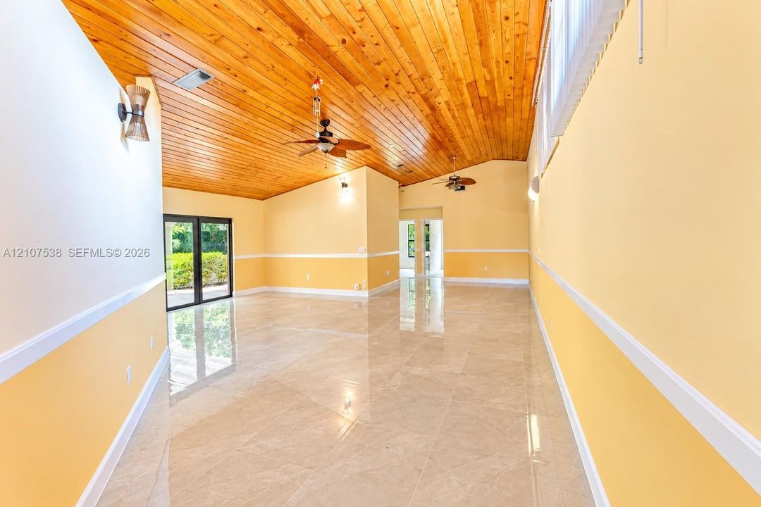 Vaulted wood-plank ceiling featuring integrated ceiling fans, large-format tile flooring, chair rail molding, and sliding glass doors