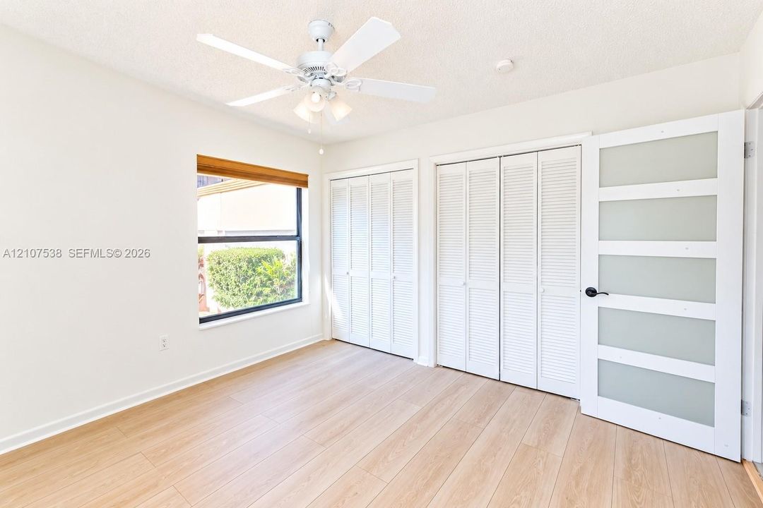 Room featuring wood-finish flooring, dual bi-fold louvered closets, a frosted glass paneled door, and a ceiling fan with integrated light fixture