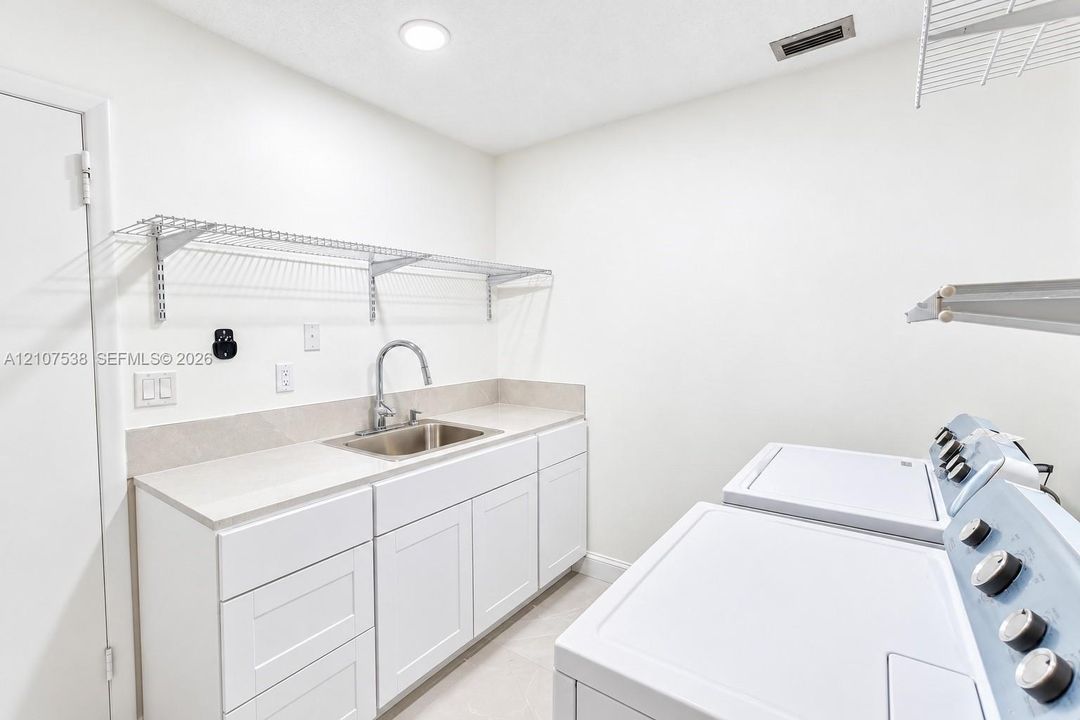 Utility room featuring white shaker-style cabinetry, solid-surface countertop, stainless steel drop-in sink with gooseneck faucet, and white wire wall shelving