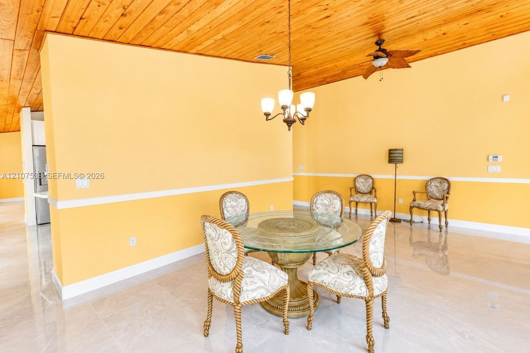 Vaulted tongue-and-groove wood ceiling, polished tile flooring, white chair rail molding, and multi-light hanging chandelier