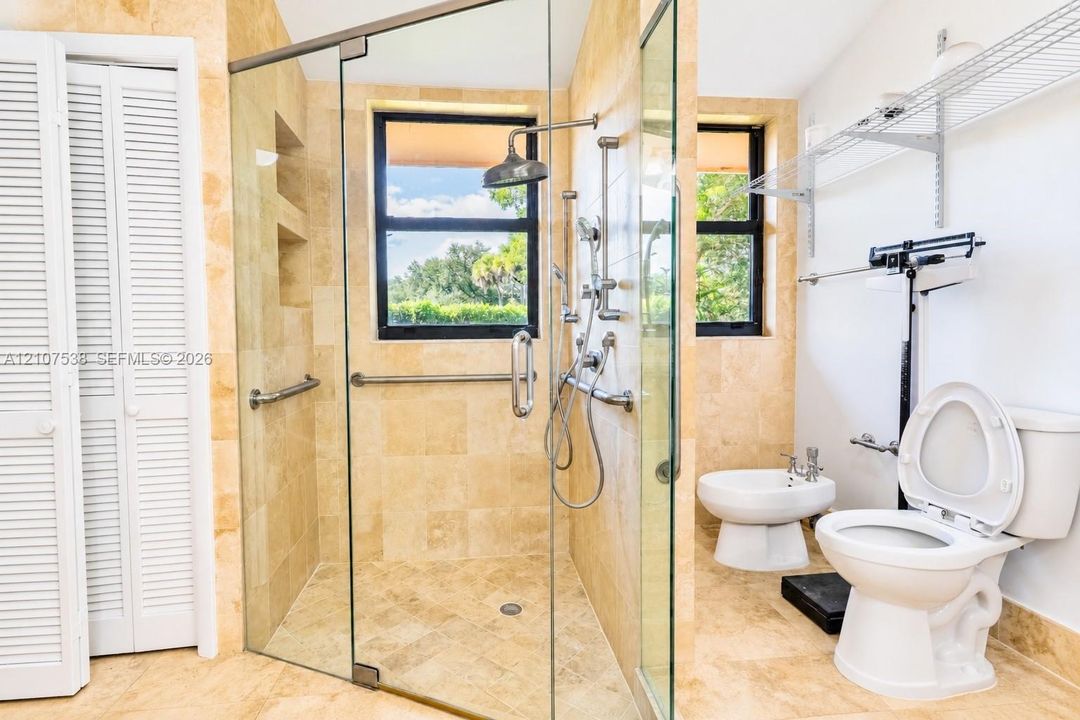 Walk-in shower featuring natural stone tiling, a glass enclosure, and a multi-head shower system with wall-mounted grab bars