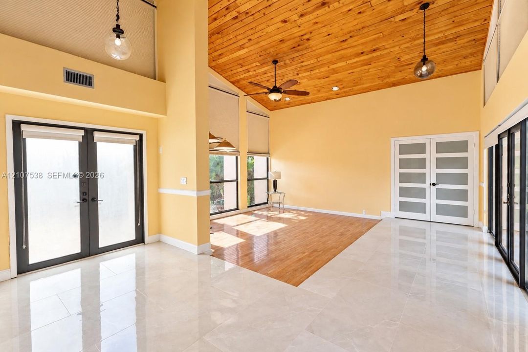 Vaulted tongue-and-groove wood ceiling, polished stone-finish flooring, wood-finish flooring inlay, double-glass paneled doors, and multi-paned floor-to-ceiling windows