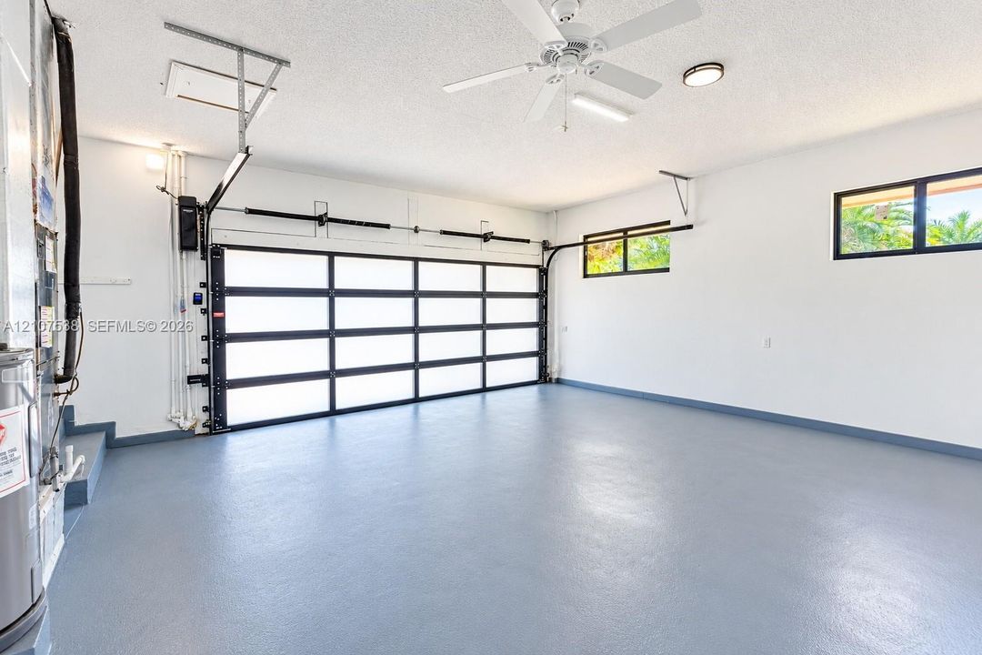 Multi-pane glass panel garage door, epoxy-coated concrete flooring, ceiling-mounted paddle fan, and dual high-set windows