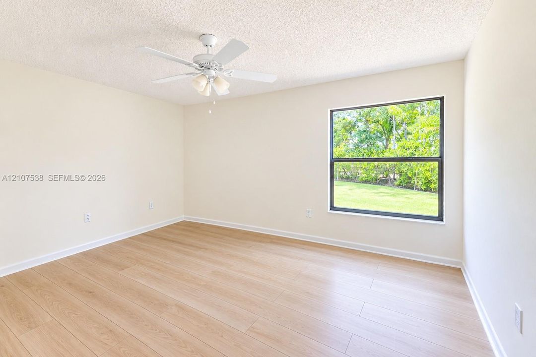 Neutral-toned interior featuring wood-finish flooring, a white ceiling fan with integrated lighting, and a large single-pane window