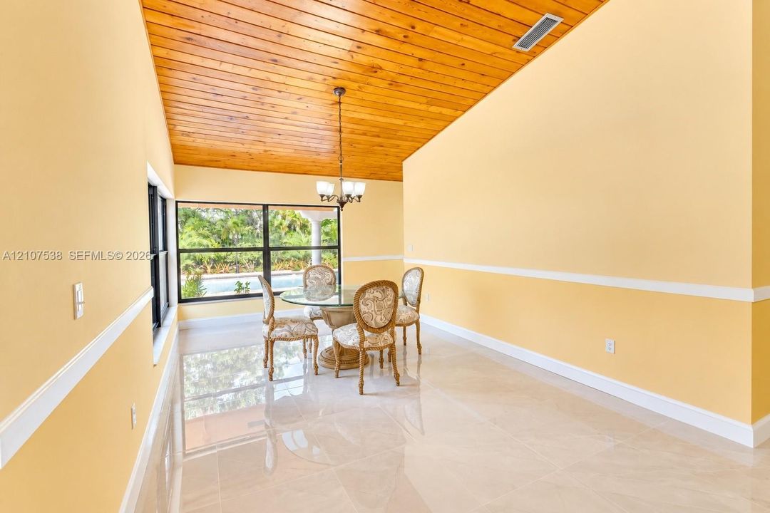 Vaulted wood-plank ceiling, large-format tile flooring, chair rail molding, and a suspended multi-light chandelier