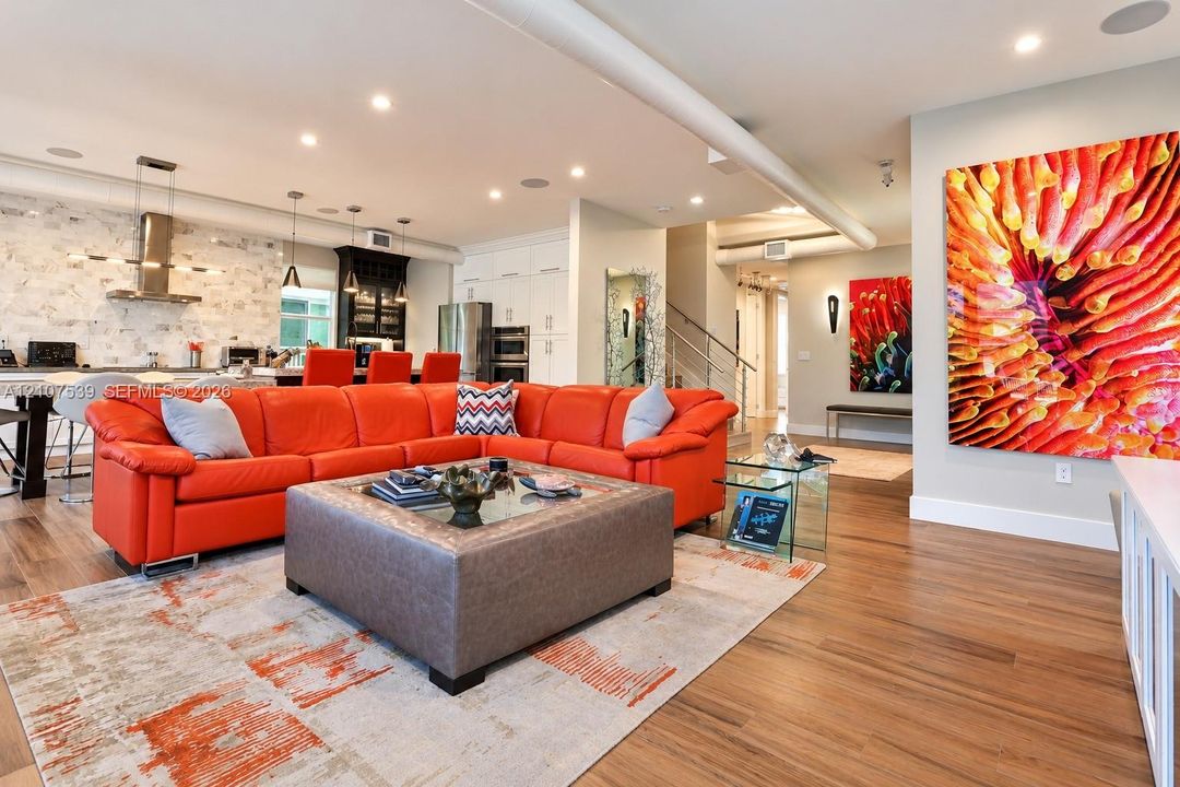 Open-concept interior featuring wood-finish flooring, recessed lighting, a stainless steel range hood, stone-style backsplash, and white cabinetry