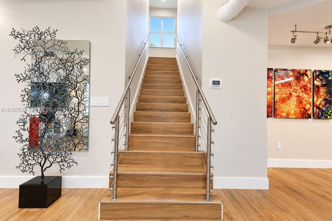 Staircase featuring wood-finish treads, stainless steel cable railings, and a metal handrail