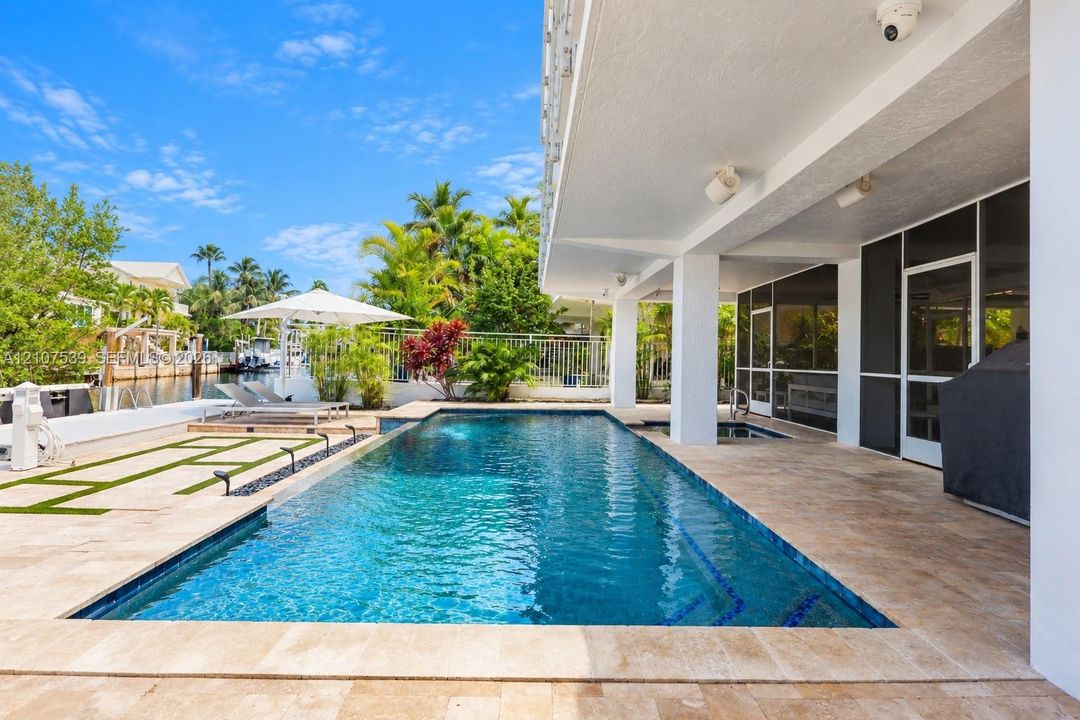 In-ground pool with tiled waterline and stone decking, covered patio, integrated spa, and waterfront bulkhead