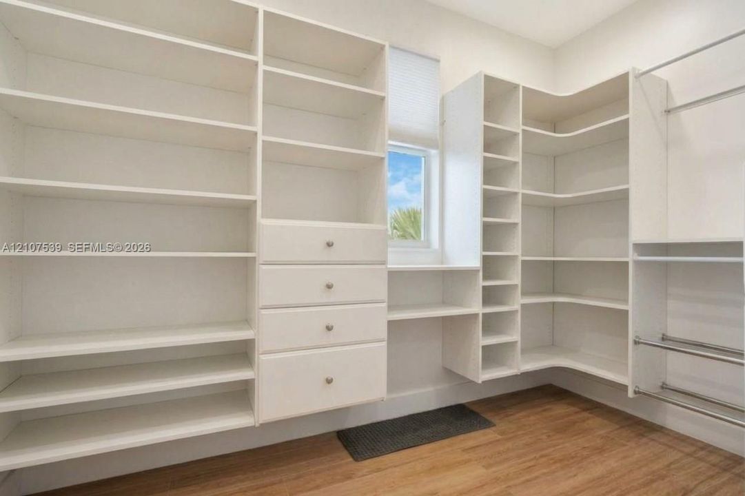 Custom white built-in shelving featuring floor-to-ceiling storage, integrated drawer units with metallic hardware, corner shelving, and metal hanging rods over wood-finish flooring